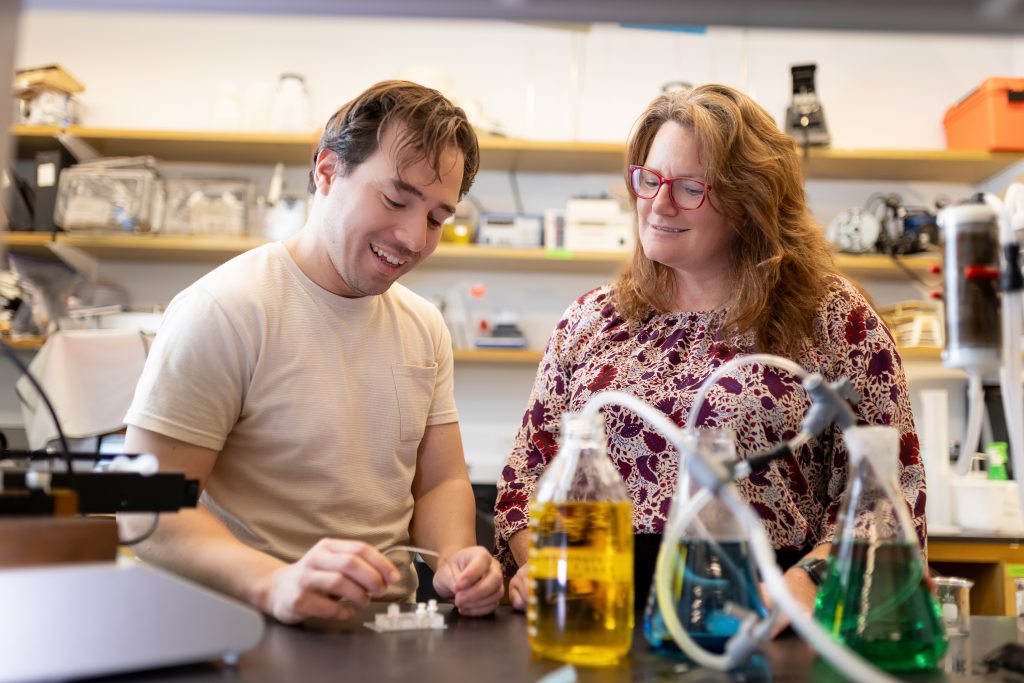 Two individuals conducting an experiment in a lab with bottles of colorful liquids.